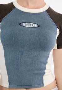Top fitted blu e crema con maniche raglan marroni, texture a costine e logo ricamato "Guess Originals" sul davanti.