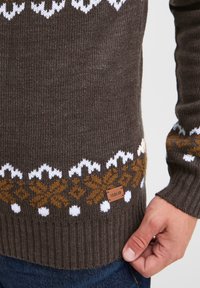 Maglione marrone lavorato a maglia con motivi geometrici bianchi e arancioni. Polsini e orlo a costine, con una piccola etichetta in pelle etichettata "ISOLID."