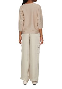 Beżowa bluzka z 3/4 rękawem w połączeniu z szerokimi, kremowymi spodniami z bocznymi kieszeniami. Tkanina wydaje się być miękka i lekka.