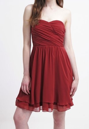 Robe rouge bustier froncée avec jupe en chiffon superposée portée par une personne aux longs cheveux bruns sur fond blanc.