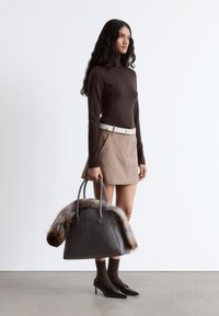 Brown turtleneck top, beige skirt with pockets, holding a gray handbag with fur accents. Black high heels and textured brown socks.