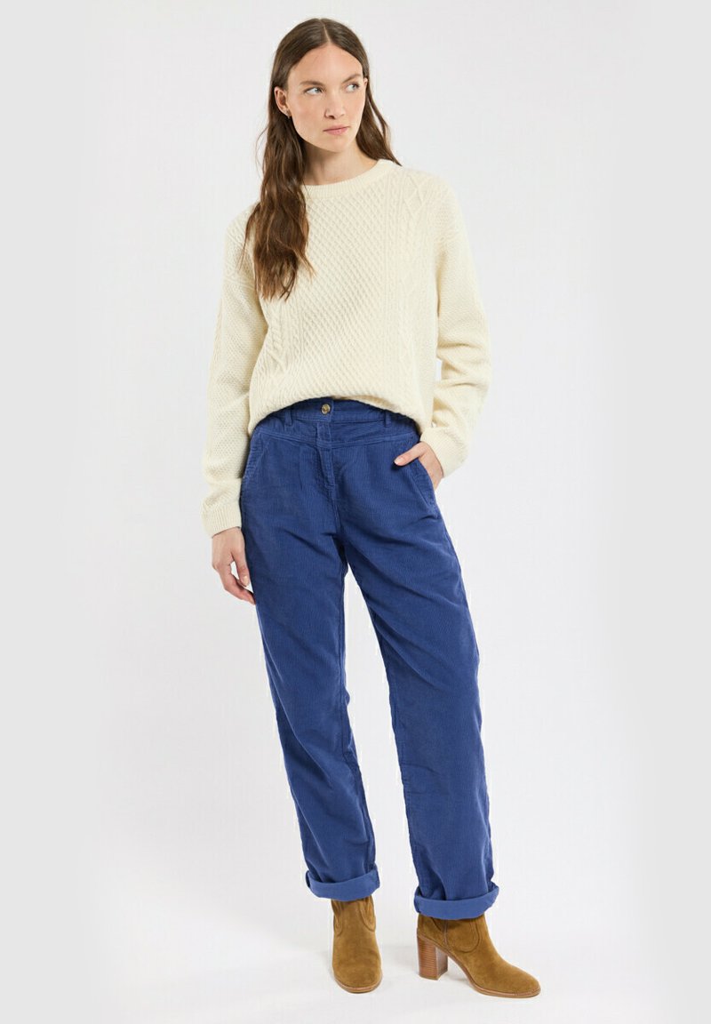 Pull en maille torsadée crème, pantalon en velours côtelé bleu avec les poignets retroussés et bottines à talons beige. Design simple et texturé avec une coupe décontractée.