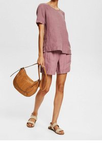 Ensemble chemise à manches courtes en lin rose clair et short, associé à un sac à main en cuir marron avec une forme incurvée et des surpiqûres contrastantes.