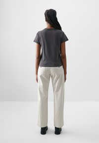 Grå kortärmad t-shirt med rund halsringning, parat med löst sittande ljusbeiga byxor och svarta ankelboots. Diskreta märkessymboler är synliga.