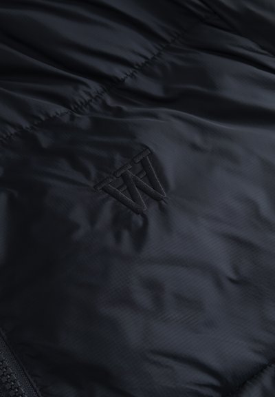Black padded fabric with stitched overlapping letters "W" and "N" in the center, featuring visible zipper on the left side.