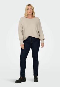 Light beige, ribbed long-sleeve top with a wide neckline, worn over dark blue skinny jeans. Black platform shoes complete the outfit.