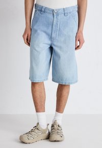 Jasnoniebieskie szorty dżinsowe o luźnym kroju, z zapięciem na guzik i podwiniętymi nogawkami. Noszone z beżowymi trampkami i białymi skarpetkami do kostek.