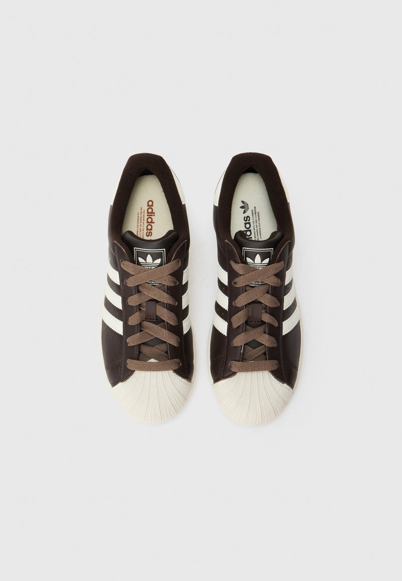 Coppia di sneakers Adidas marroni con punte bianche a conchiglia e tre strisce bianche, viste dall'alto su sfondo bianco.