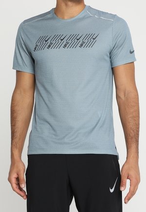 Homme portant un t-shirt Nike bleu clair avec un logo noir et un motif rayé sur la poitrine et un short Nike noir avec un swoosh blanc.