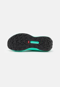 Bėgimo batelių padas su juoda guma ir turquoise spalvos tarpinė, taip pat raudonas akcentas trikampio formos šalia kulno.