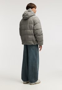 Siva puffer jakna s kapuco, z oštebnimi paneli, ohlapen kroj in elastičnimi manšetami. Dopolnjena z širokimi denim hlačami in belimi športnimi copati.