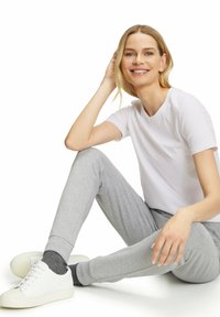 Witte katoenen t-shirt gecombineerd met grijze sweatpants. Model draagt witte sneakers en grijze sokken, zittend met één hand op haar hoofd. Eenvoudig ontwerp.