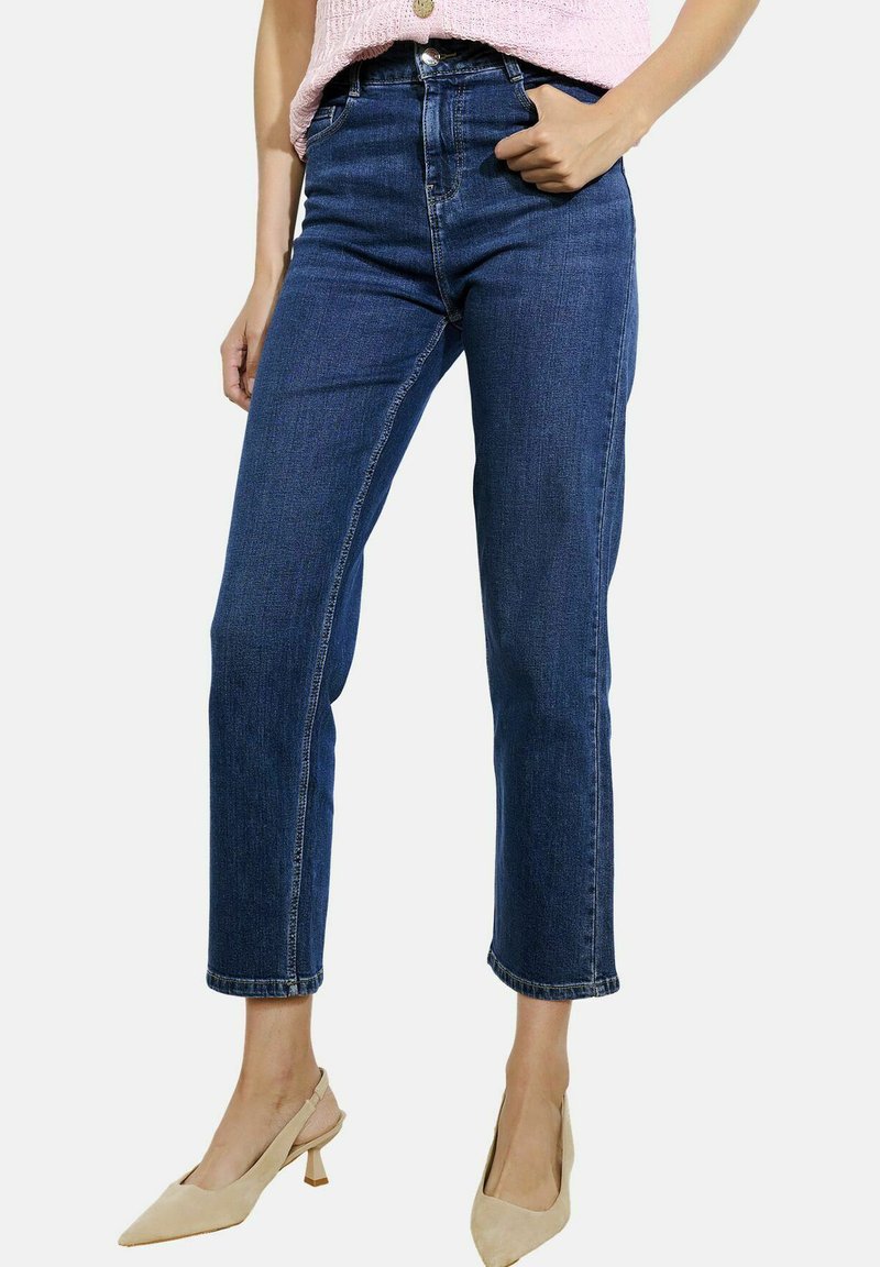 Tumed sinised denim teksad sirge lõikega, kõrge vöökoha ja lühikese pikkusega, millel on vööaasad ja nähtavad õmbluse detailid.