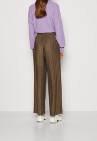 Wijdvallende, geplooide bruine broek met een elastische tailleband. Combinatie met een lichtpaarse trui en witte sneakers. Zachte textuur.
