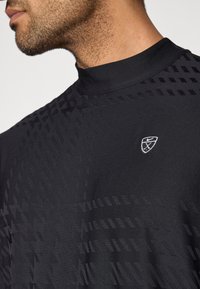 Μαύρο αθλητικό πουκάμισο με ψηλό λαιμόκομμα, με υφασμένο γεωμετρικό μοτίβο και μικρό κεντημένο λογότυπο στο στήθος.