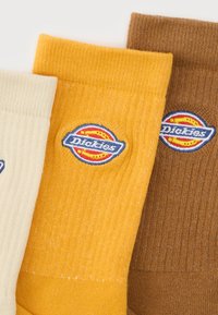 Τρία διπλωμένα ριγωτά κάλτσες σε κρεμ, μουσταρδί κίτρινο και καφέ με κεντημένες ετικέτες λογότυπου Dickies.