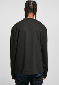 Long-sleeve, dark green cotton shirt with a relaxed fit, crew neck, and drop shoulders. Smooth texture and simple design, no visible patterns.