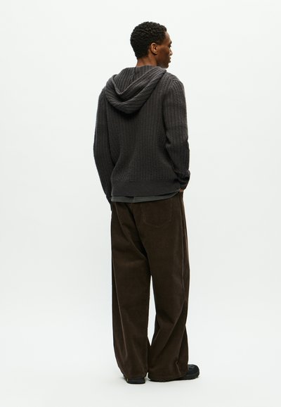 Sudadera de punto acanalado en gris oscuro, con capucha, combinada con pantalones de pana marrones y sueltos. El conjunto presenta un aspecto relajado y texturizado.