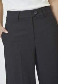 Pantaloni neri su misura con una texture liscia, caratterizzati da una chiusura con bottone frontale, tasche laterali e un design a gamba dritta.