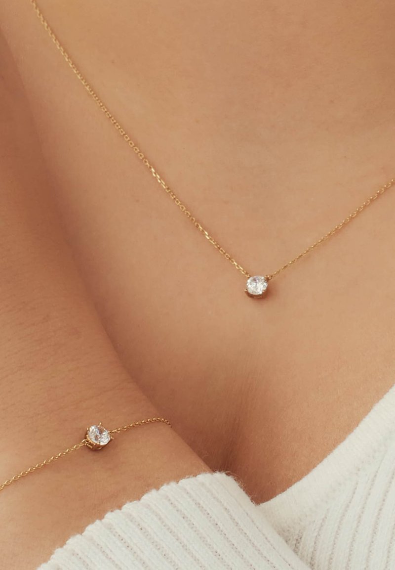 Kette mit goldfarbener Beschichtung und einem einzelnen runden klaren Kristallanhänger. Glatte Textur, dünnes Design und zarte Glieder.