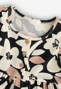 Robe côtelée à col rond avec un grand imprimé floral noir, blanc et rose, avec trois boutons en bois sur la patte de boutonnage avant.