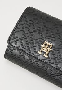 Zwarte gestructureerde portemonnee met een reliëfpatroon, gouden hardware logo-accent en gestikte randen. Compacte rechthoekige vorm.