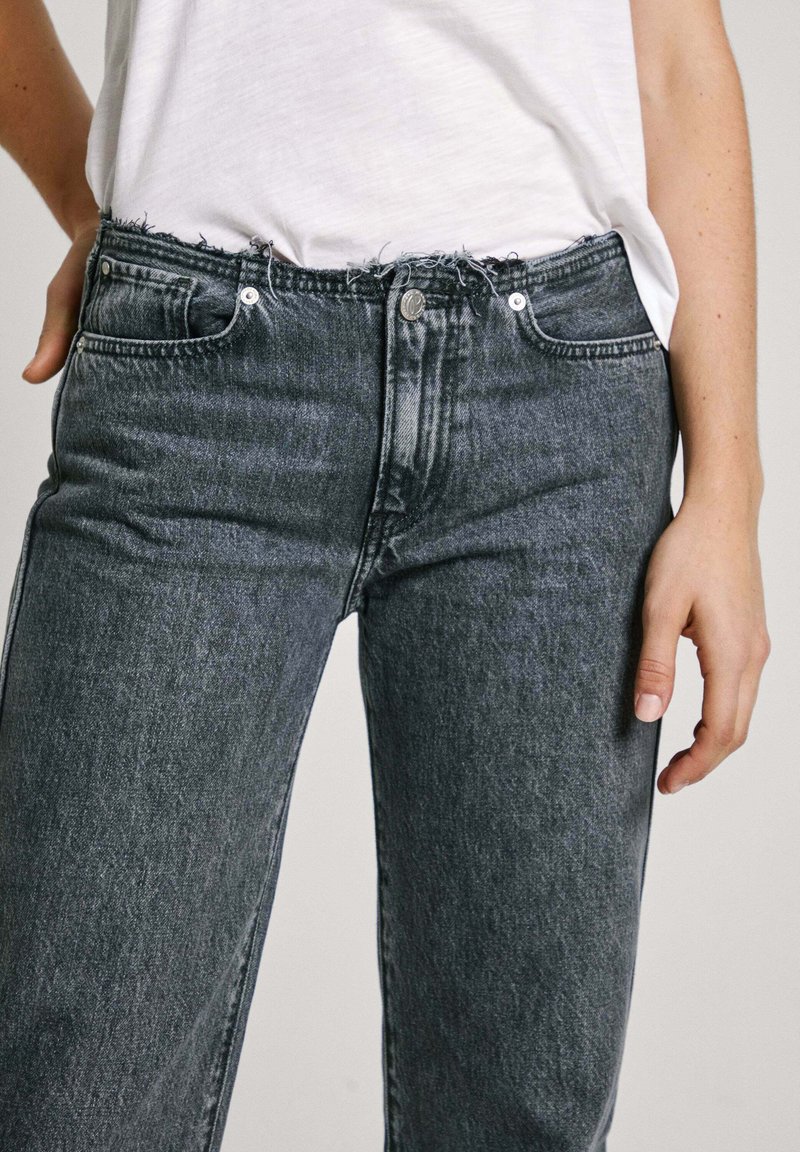 Hochtaillierte, schwarze Denim-Jeans mit fransigem Saum, Fünf-Taschen-Design und Knopfverschluss vorne. Matte Oberfläche mit subtiler Textur.