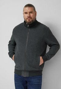Dark gray zip-up jacket with a textured pattern, high collar, and ribbed cuffs. Paired with blue jeans. Material appears soft and thick.