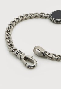 Ασημένιο μεταλλικό βραχιόλι αλυσίδα με στρογγυλό μαύρο κέντρο και διακοσμητικά με χάντρες. Διαθέτει κλιπ και γυαλισμένους κρίκους.
