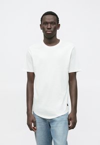 Bílý krátký rukáv tričko s kulatým výstřihem, vyrobené z měkké bavlny, se rovnými lemy a malou logo nášivkou na boku.