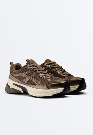 Paar braune Sportschuhe mit Obermaterial aus Mesh und Synthetik, weißer klobiger Sohle und schwarzer Profilsohle, schräg gestellt, um die Außenseiten zu zeigen.