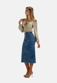 Beige off-shoulder top med bindedetalje og smocktalje, kombineret med en tætsiddende blå denim midi-nederdel og klare hælsandaler.