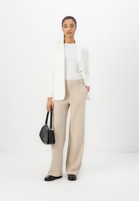 Hvit blazer over en hvit skjorte, beige vide bukser og svart håndveske. Glatte materialer, skreddersydd design og nøytral fargepalett.