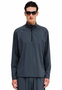 Donkergrijs, lange mouwen sporttop met een ritskraag en textuurstof. Heeft een relaxte pasvorm en minimale merkdetail.