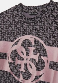 T-shirt a maniche corte di colore viola con un motivo a logo nero ripetuto e una grande grafica logo rosa sulla parte anteriore. Design con scollo tondo.