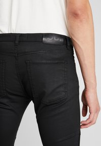 Jeans de mezclilla negra con un diseño ajustado, que presentan un parche de logo de cuero en la parte posterior, costuras en contraste y dos bolsillos traseros.