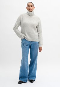 Light gray knit turtleneck sweater with a relaxed fit, paired with high-waisted, flared blue jeans and black shoes. Simple design, soft texture.