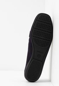 Marineblaue Wildlederschuhe mit einer schwarzen Gummisohle, die ein durchbrochenes Design, das Geox-Logo und eine abgerundete Zehenpartie aufweisen. Vor einem weißen Hintergrund platziert.