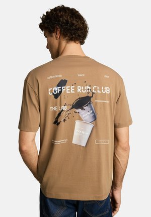 Homme portant un t-shirt marron avec un motif éclaboussure de café et le texte "Coffee Run Club" dans le dos, tourné de dos à la caméra.