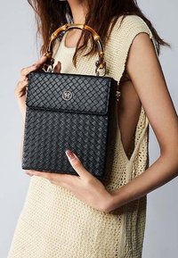 Czarna pleciona torebka o prostokątnym kształcie, z bambusowym uchwytem i frontowym zatrzaskiem z logo. Szczegóły teksturowanej powierzchni ze skóry.