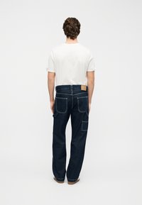 Σκούρο μπλε τζιν με άνετη εφαρμογή, διαθέτει πίσω τσέπες, τσέπη cargo και καφέ δερμάτινο ταμπελάκι στη ζώνη μέσης.