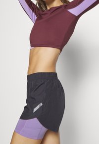 Maroon lyhytcropped pitkähihainen paita, joka on yhdistetty mustiin ja laventelin värisiin shortsihousuihin, joissa on sivussa geometrinen kuvio ja joustava vyötärö.