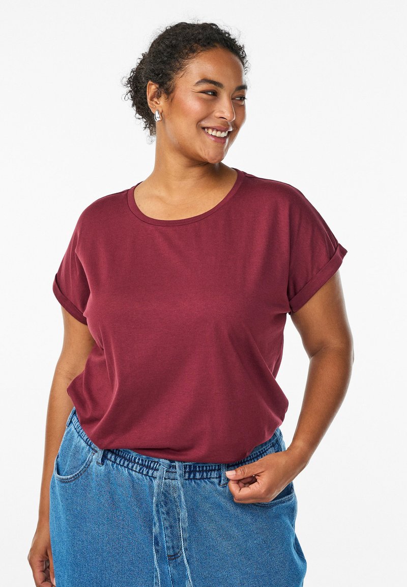 Vino rdeča kratka majica s kratkimi rokavi in krožnim ovratnikom, mehko teksturo in zavitimi rokavi, v kombinaciji z modrim jeans krilom z opaznim pasom.