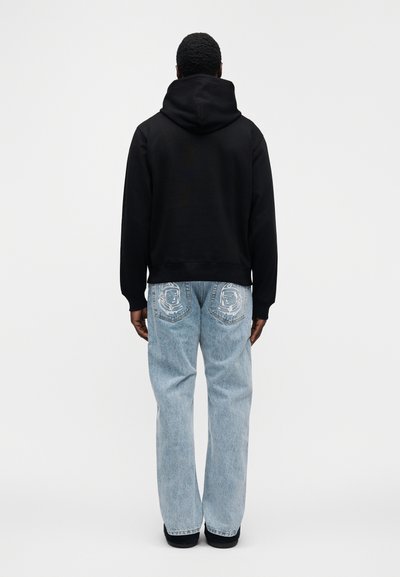 Μαύρο φούτερ με κουκούλα και άνετη εφαρμογή, συνδυασμένο με ανοιχτόχρωμο τζιν παντελόνι με κεντητά σχέδια στις πίσω τσέπες.