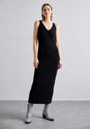Black knit sleeveless dress with a V-neck, fitted silhouette, and mid-calf length. Paired with grey ankle boots.