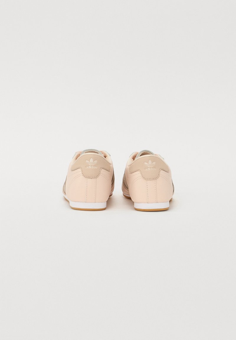 Zapatillas rosa claro con una textura de cuero suave, con acentos beige, suelas blancas y un logotipo distintivo en la parte posterior.