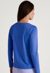 Blauwe lange mouwen shirt met een bootnek, gladde textuur en een eenvoudig ontwerp. De achteraanzicht toont een getailleerde silhoeet en minimale naden.