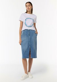 White t-shirt with blue and pink circular text graphic, paired with a knee-length, light blue denim skirt featuring front slit and pockets.
