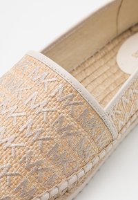 Chaussure espadrille tissée beige avec un motif de logo "MaxMara" cousu en taupe clair et une bordure en cuir blanc autour de l'ouverture.
