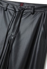 Pantalons en simili cuir noir avec une texture lisse, dotés d'une fermeture à bouton, d'un cordon de serrage et de coutures ajustées pour une silhouette près du corps.
